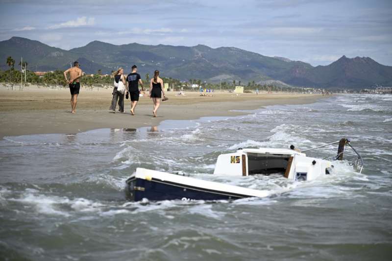 Varias personas pasan junto al velero varado en la playa del Pinar de Castelln. EFEAndreu Esteban