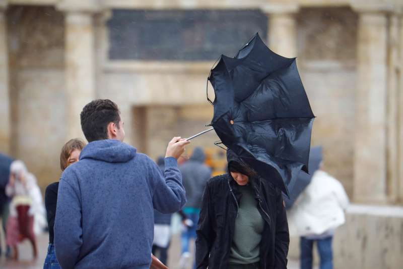 Unos turistas intentan protegerse del viento y de la lluvia con un paraguas. EFE/Salas/Archivo
